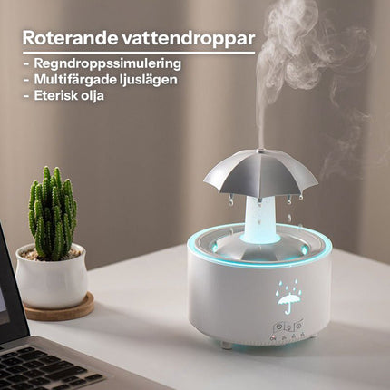 Vit aromadiffuser med roterande vattendroppar och LED-ljus på skrivbord bredvid laptop och kaktus